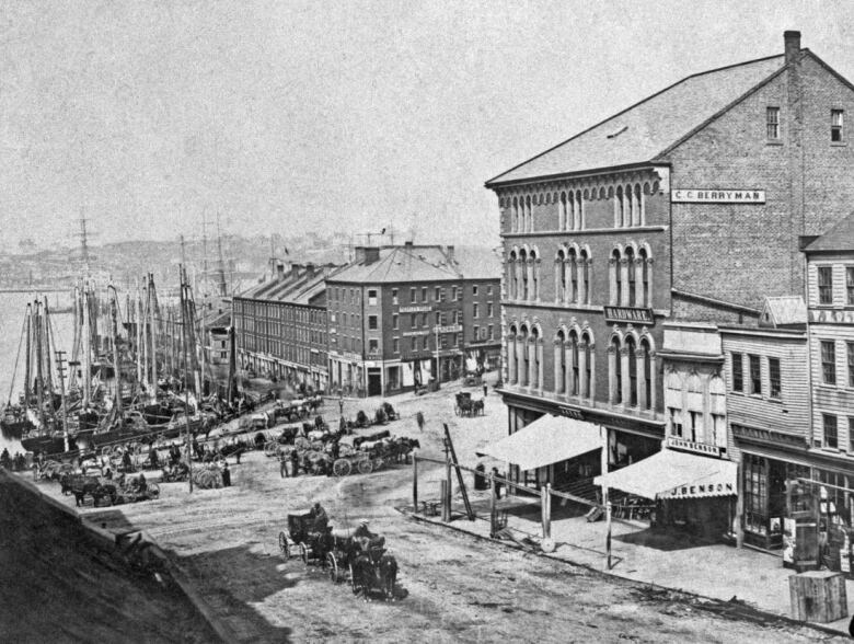 black and white photo of busy scene at Market Slip in Saint John with boats tied up 