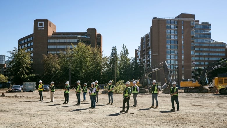 People in hard hats and hi-viz vests stand in a dirt lot during a groundbreaking ceremony for the Senakw development in Vancouver.