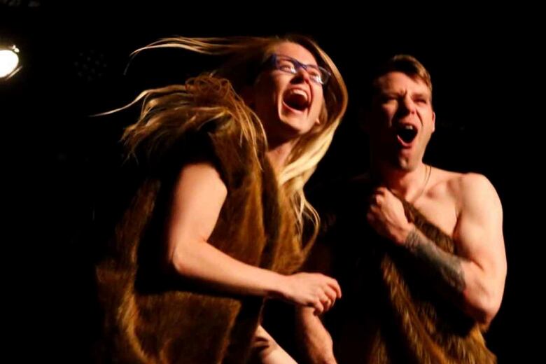 Two people dressed in animal skin laugh on a stage.