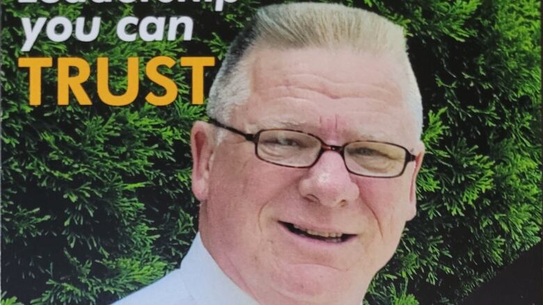 A close up of a man's head in front of some spruce bushes. He has white hair and glasses. The words 