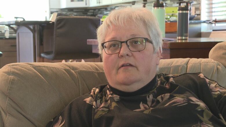 Woman with glasses sits on a couch.