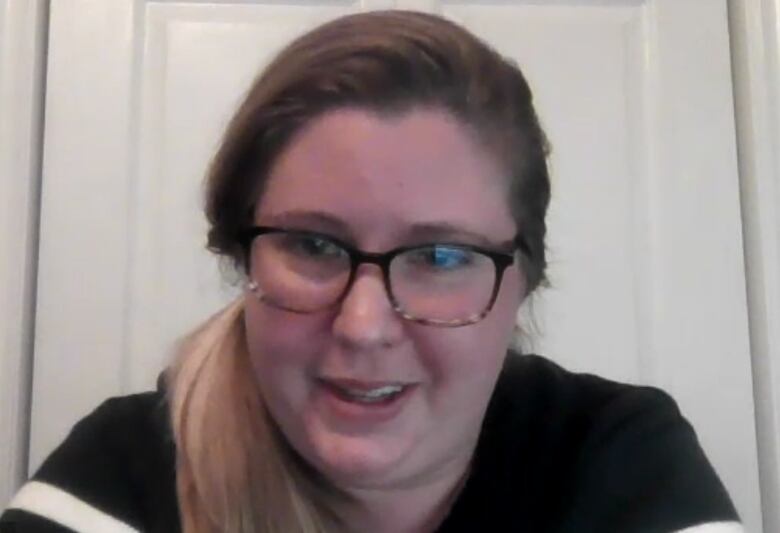 A woman with glasses looks into the web camera on her laptop.