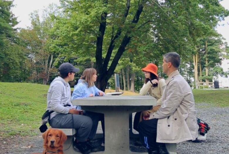 Four people sit around a stone table in a large park. 