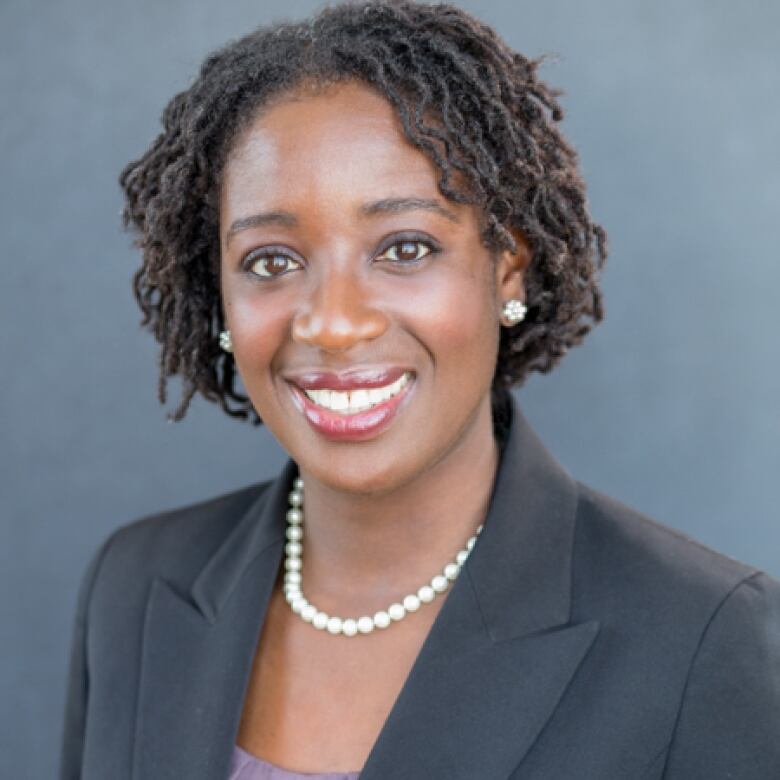 A smiling woman wearing a string of pearls around her neck and a suit jacket smiles for a portrait photo.