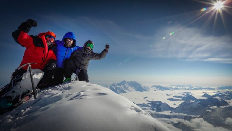 Three people posing at the peak of a snowy mountain on a blue sky, bright sun day.