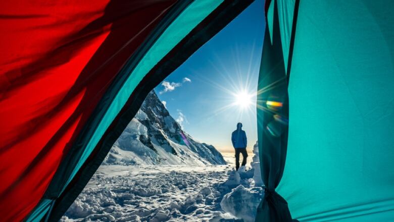 A glimpse of a man standing on a snowy mountain with the sun shining from the perspective of inside of a tent.