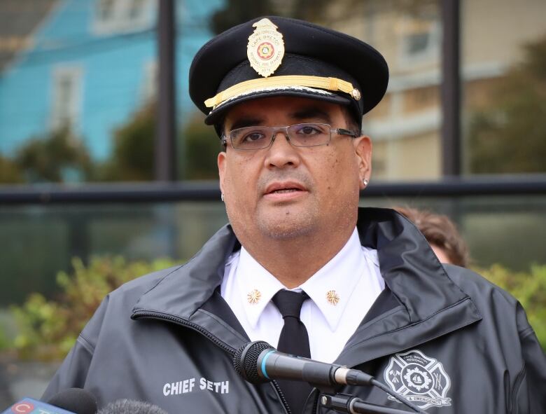 A man in a fire chief's hat stands at a microphone in front of city hall.