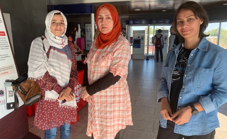 Three women stand in a train station. 