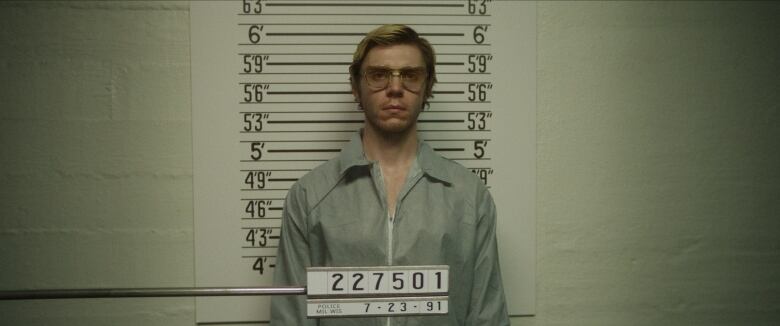 A man in glasses stands in a  police mug shot