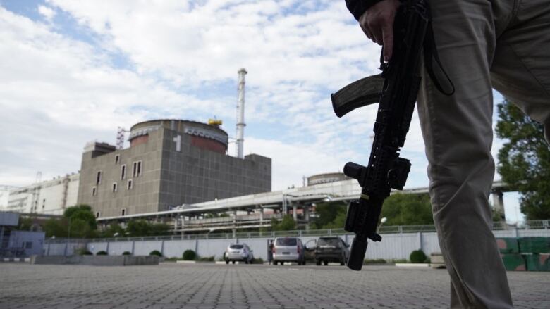 A man carries a gun in front of a nuclear plant.