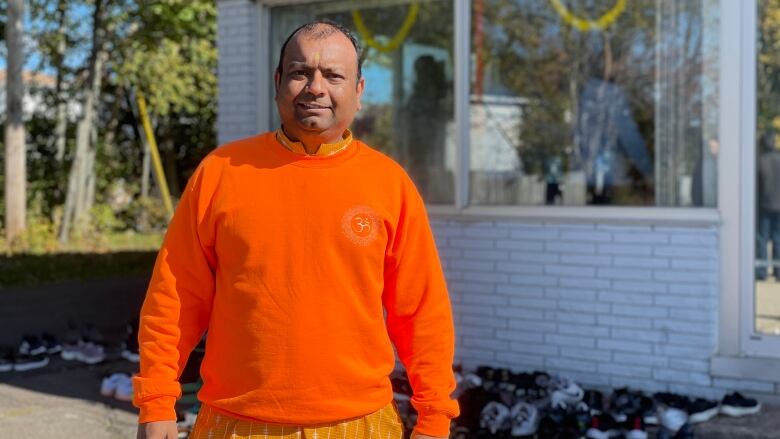 A man in a bright orange sweather stands outside in the sun.