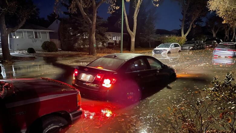 Cars are partially submerged in a street full of water.