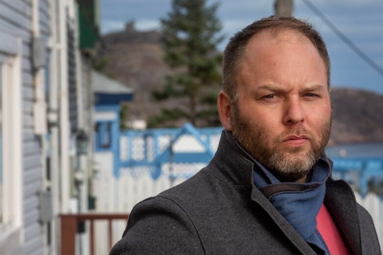 A man wearing a grey jacket looks into the camera. He has short hair and a short beard.