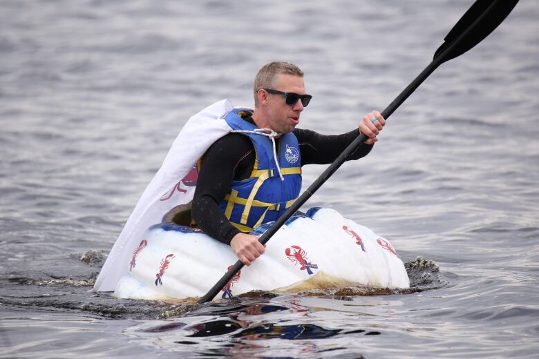 A man sits inside a giant pumpkin and paddles it through the water. 