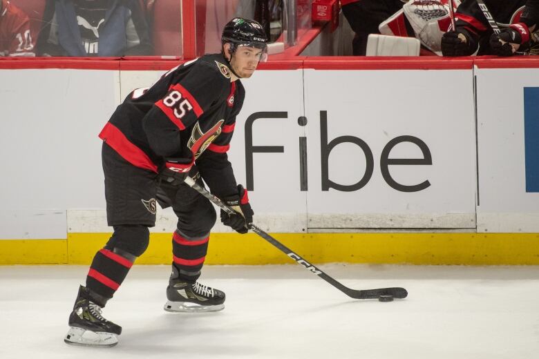 A hockey player in a black and red uniform looks up the ice.