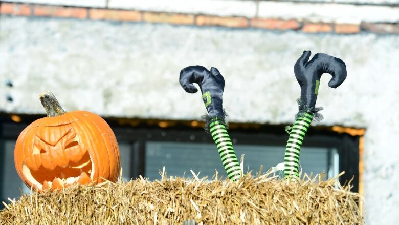 Picture of a carved pumpkin and witch legs on a block of hay.