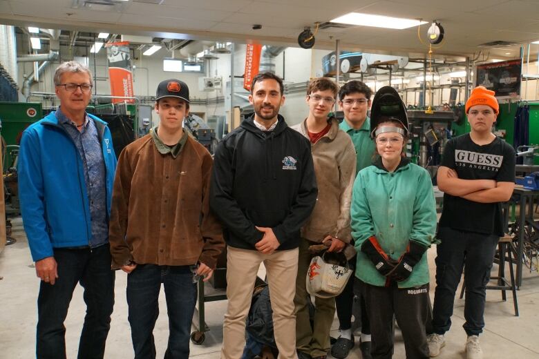 A man stands in the middle of students posing for a photo in a machine shop. 