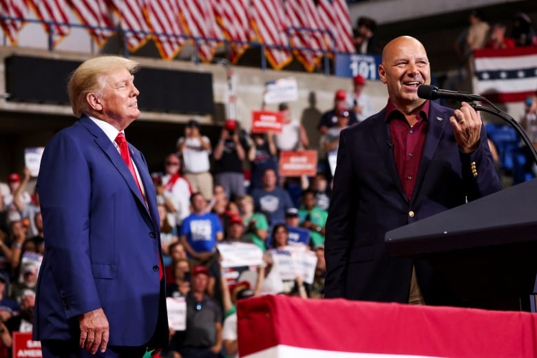 Two men stand at a rally holding microphones.