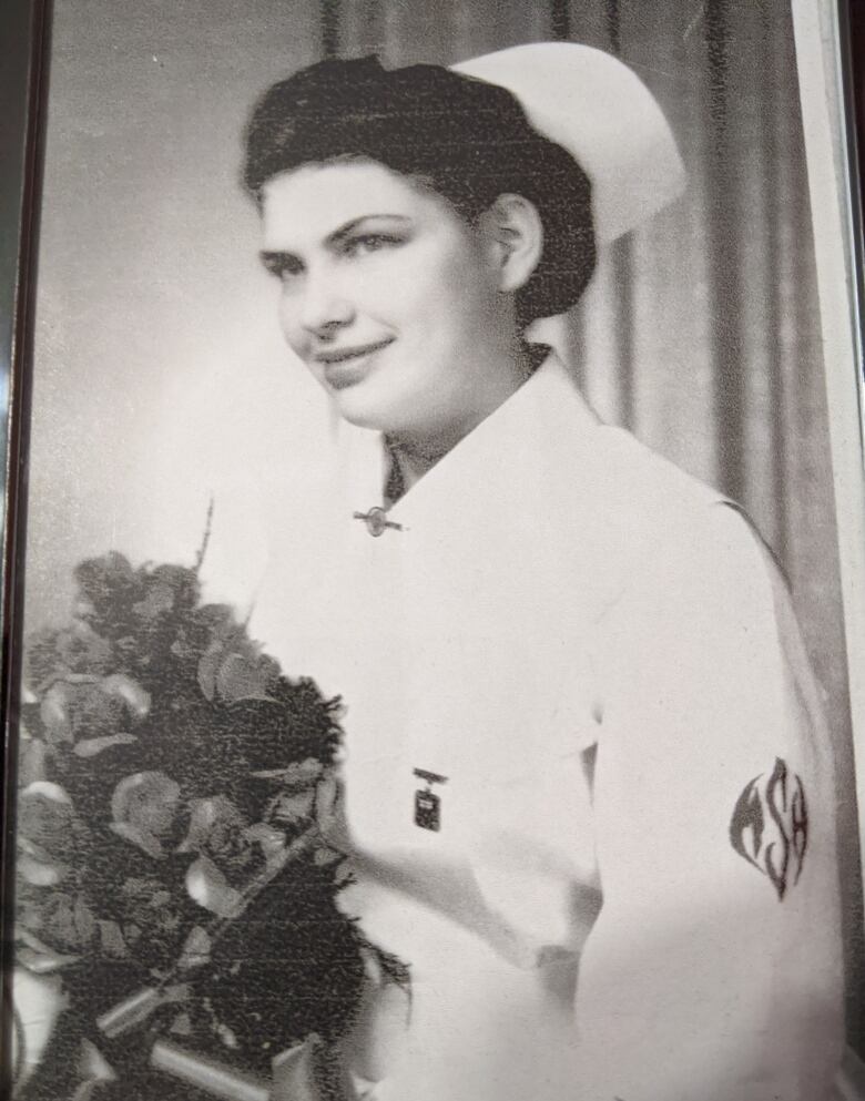 A woman wears a nursing cap and uniform holding roses in this black and white photograph. 