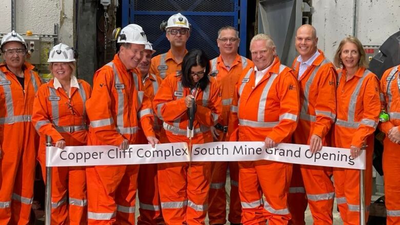 Many people in orange coveralls cutting a ribbon.