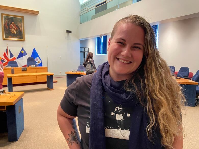 A Fredericton city councillor stands and smiles inside council chambers.