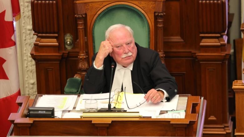 A man with white hair wearing black robes sits behind a wooden desk at the Nova Scotia legislature.