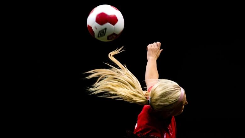 A woman soccer player wearing red makes a header.