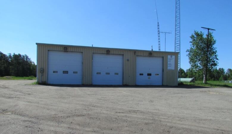 A square garage-like building with three bay doors sits in front of a gravel parking lot 