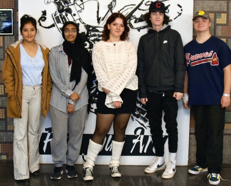 Five students standing side-by-side in the foyer of a school.