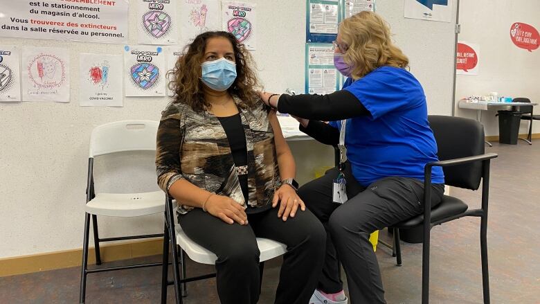 A woman receives a vaccine in the arm, administered by a nurse.