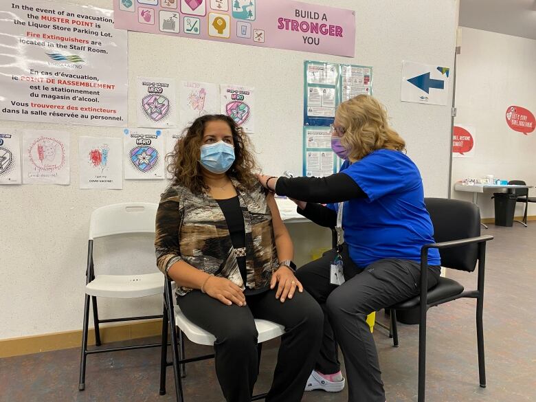 A woman receives a vaccine in the arm, administered by a nurse.