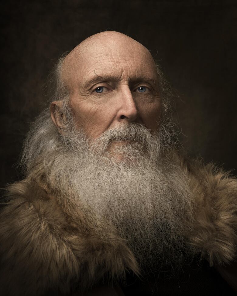 A photo of an old man, bald, with a long beard, and wearing a fur coat.