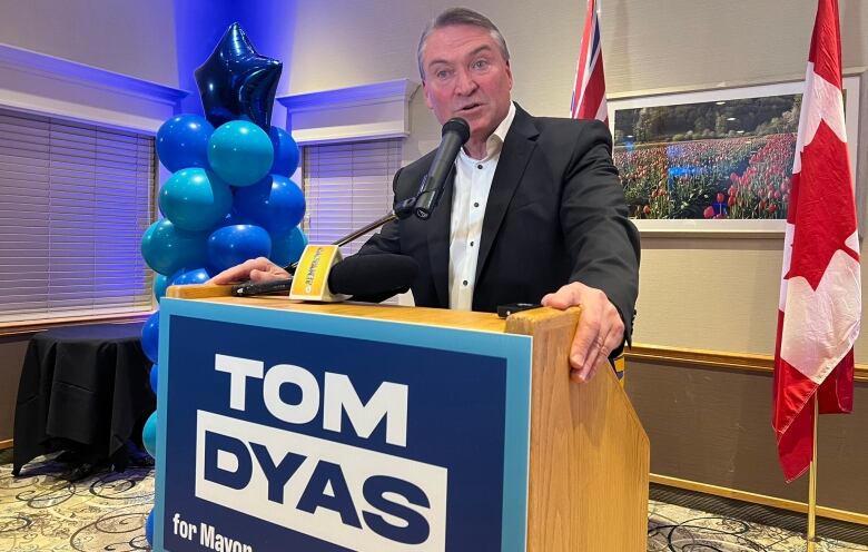 A man in black suit stands behind a podium and speaks.