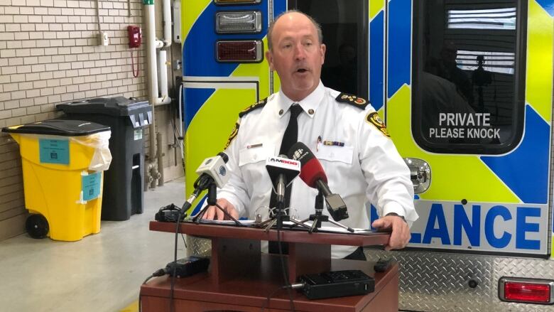 A man stands in front of a podium with an ambulance in the background.