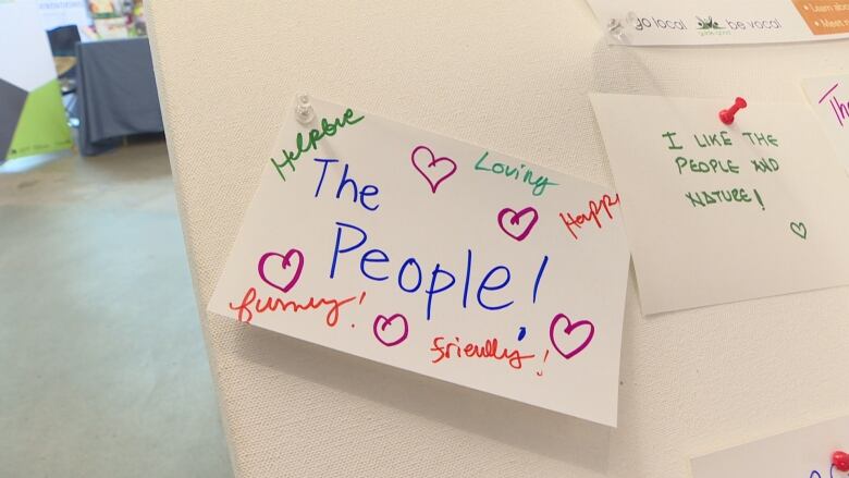 A white cue card sits tacked on a board. The middle reads 'Love the people!' with hearts around it and words like 'Funny', 'Friendly' and 'Loving'.