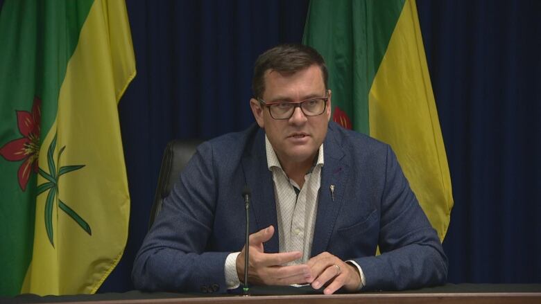 Paul Merriman sits at a table in front of a pair of Saskatchewan flags.