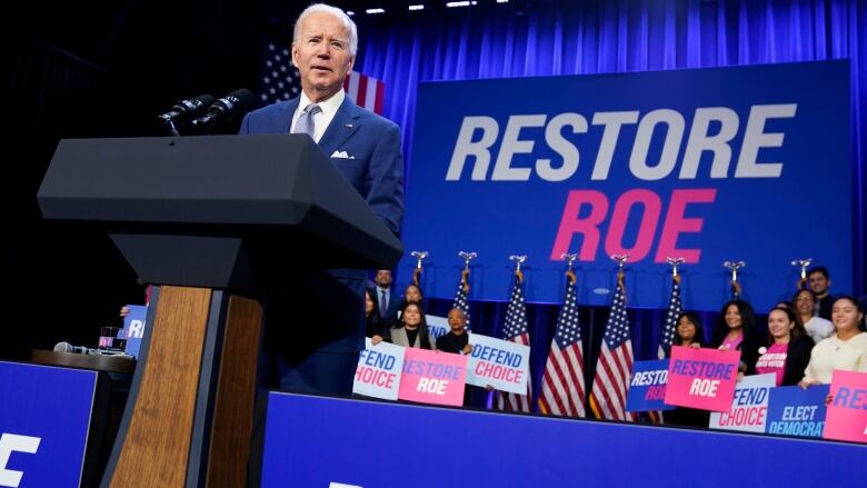 The U.S. president stands at a podium, delivering a speech, in front of a sign that reads 