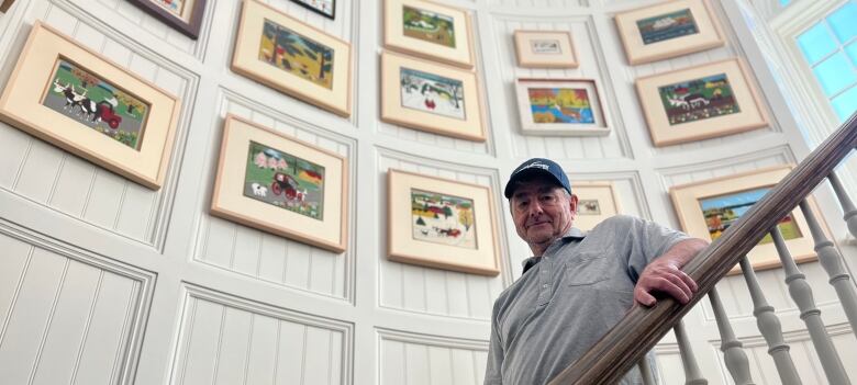 A man stands on a staircase, with paintings lining the wall.