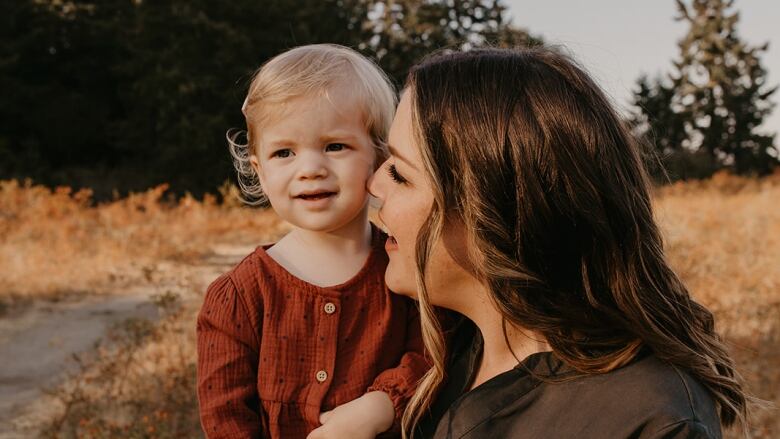 A woman holds a young child outdoors