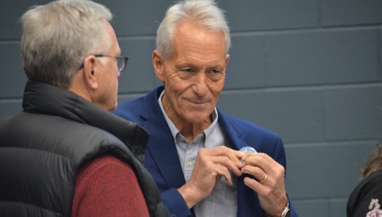 Peter Chirico affixes a campaign button to his blue blazer while speaking with another man. 