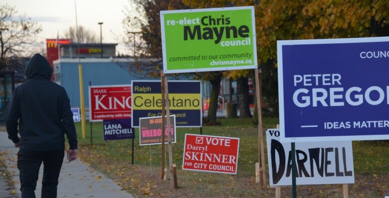 A man walks past a row of municipal election signs on Lakeshore Road in North Bay