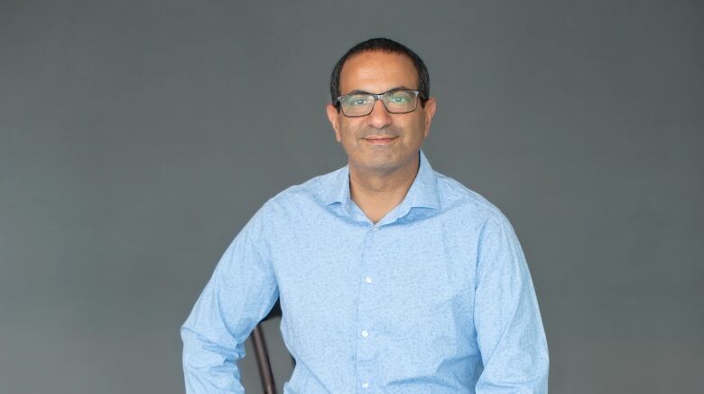 Moe Seddik sitting on a stool in a blue shirt.