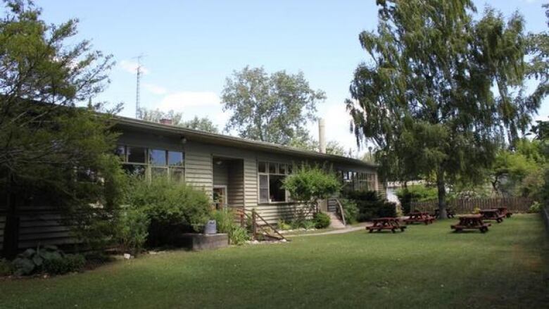 A bungalow type building surrounded by greenery and some picnic tables.