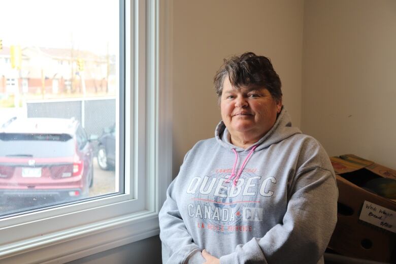 Portrait of a woman wearing a grey hoodie near a window.