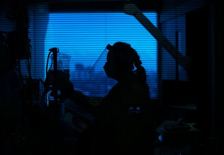 A nurse backlit against an evening or early morning sky sorts through the IV fluids and tubes for a patient. 