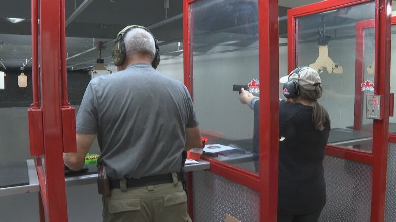 two people aim handguns in an indoor shooting range