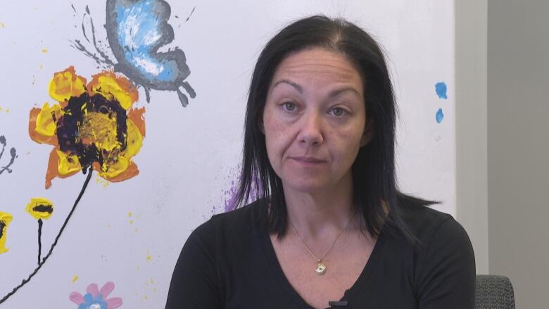 Woman sits in front of a wall with painted flowers and a butterfly. 