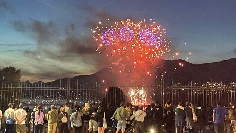 Multi-coloured fireworks explode over the ocean in Vancouver as a crowd standing on a beach watch.