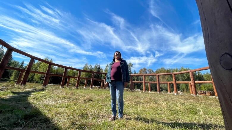 An Indigenous women stands in the middle of a large, circular powwow arbour that's under construction.