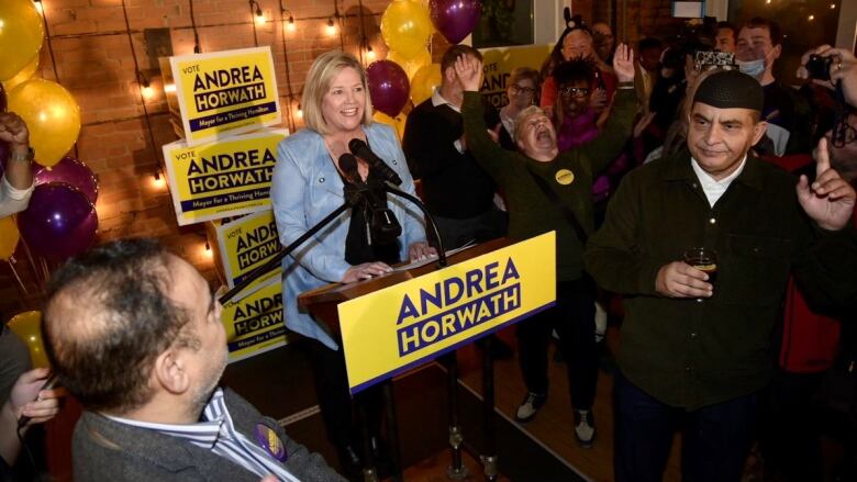 A woman standing at a podium smiling while people cheer around her.